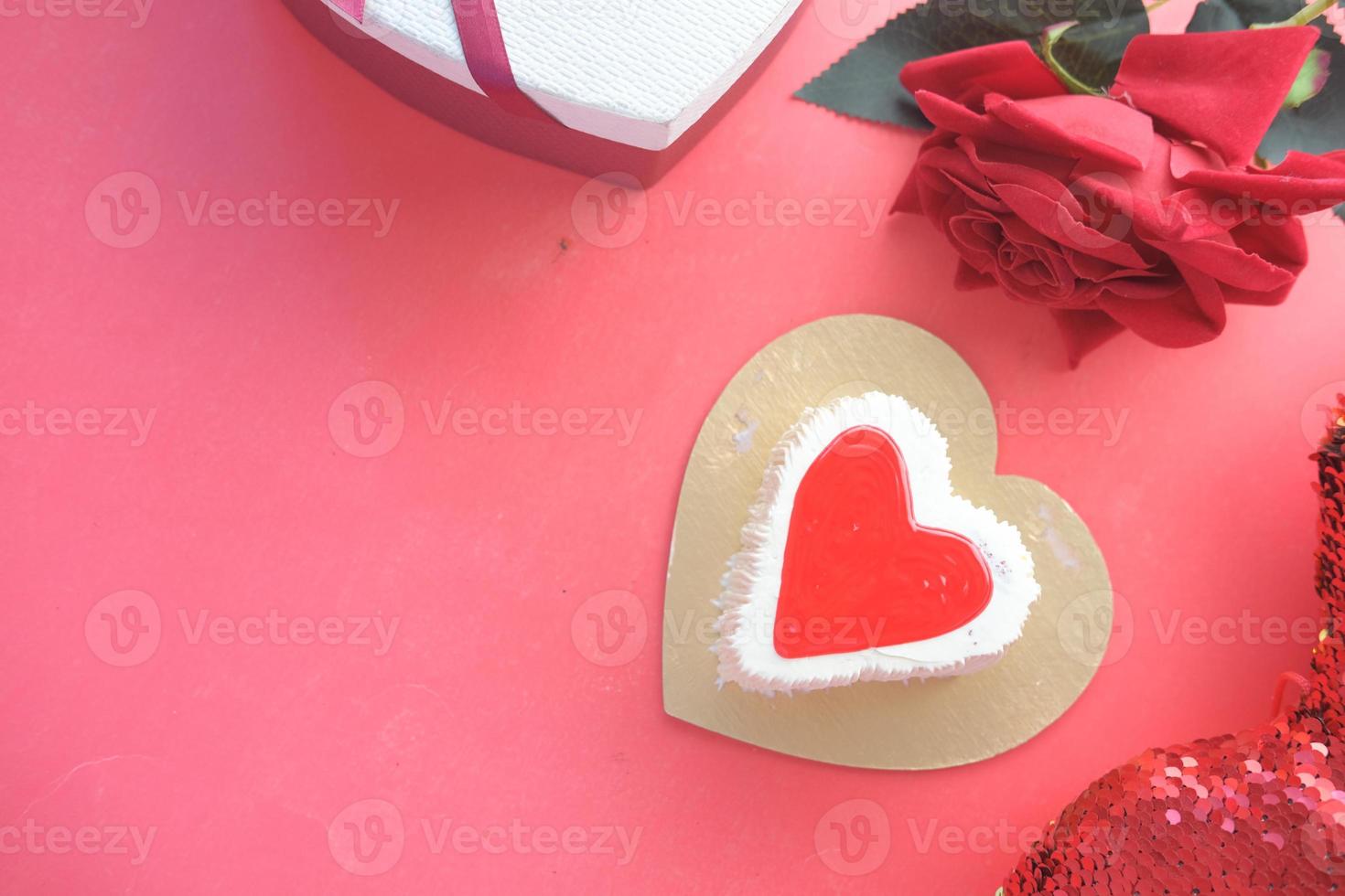 bovenaanzicht van hartvorm cake, geschenkdoos en roze bloem op rode achtergrond foto