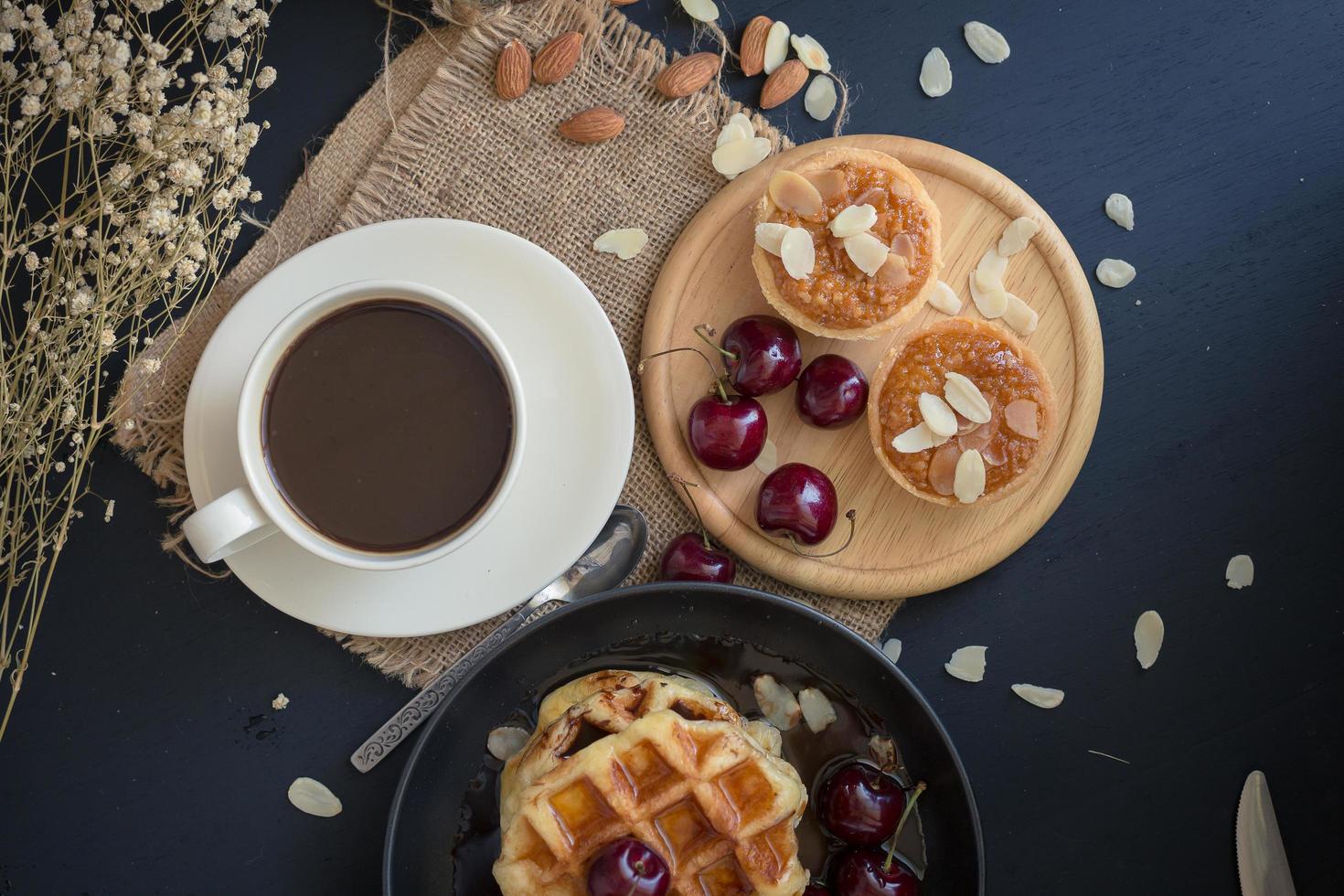 wafels en kersen met honing, knapperige amandeltaartjes en een kopje koffie op zwarte tafel foto