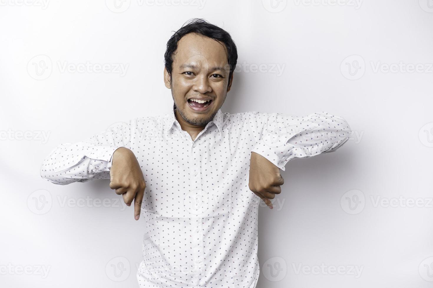 opgewonden Aziatisch Mens vervelend wit overhemd richten Bij de kopiëren ruimte hieronder hem, geïsoleerd door wit achtergrond foto