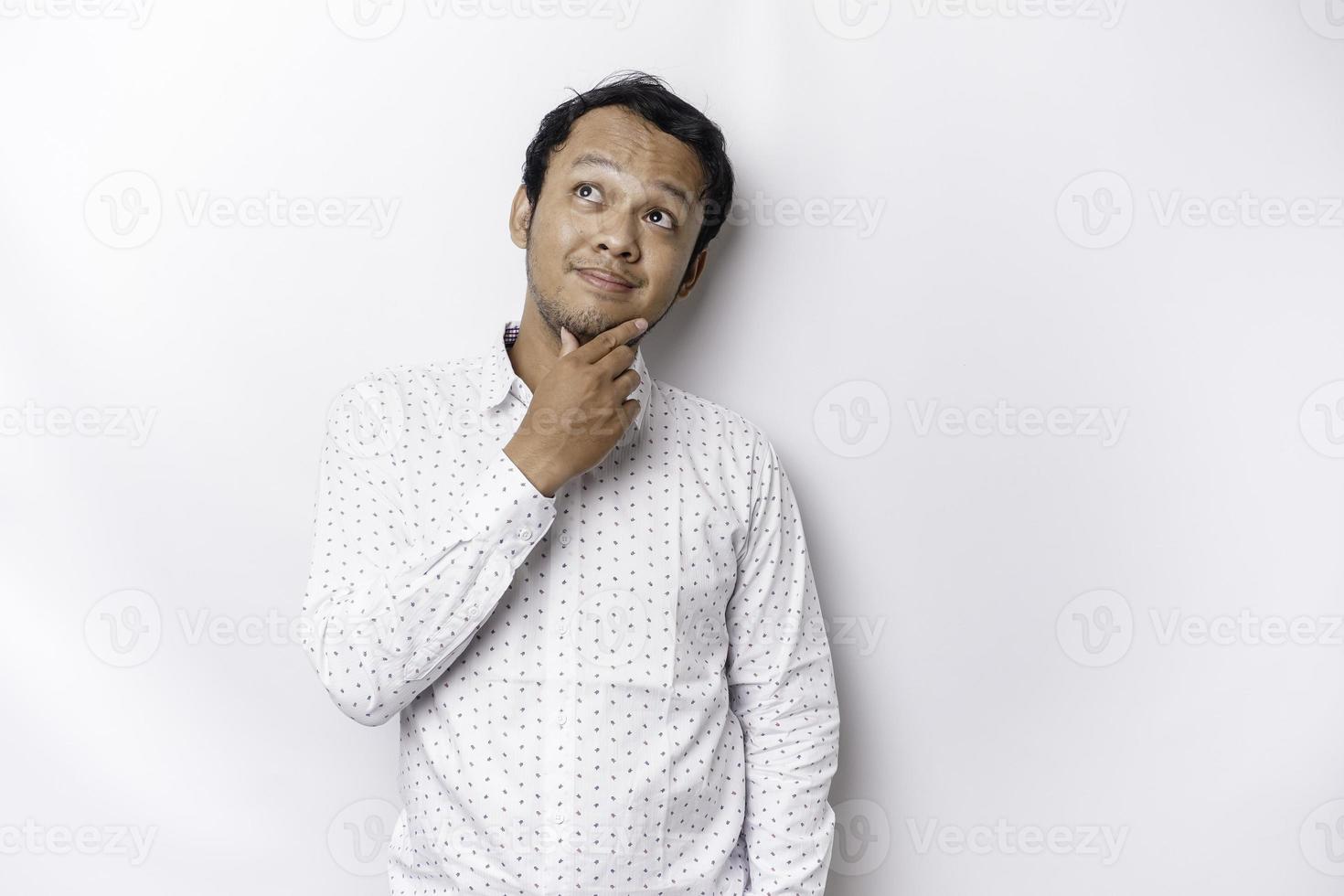 een attent jong Mens vervelend een wit overhemd terwijl op zoek terzijde, geïsoleerd door wit achtergrond foto