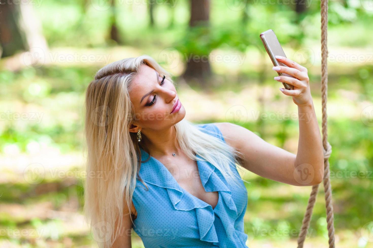 mooi blond vrouw in blauw jurk gebruik makend van smartphone naar nemen selfie foto