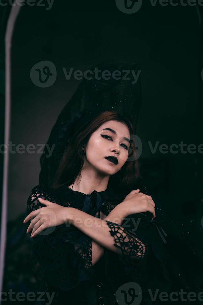 een gotisch Indonesisch vrouw vervelend een mooi zwart hoed terwijl dressing Leuk vinden een heks in zwart foto