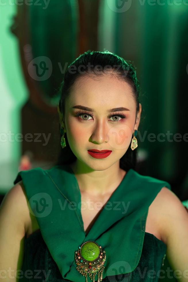 een mooi Aziatisch vrouw in een groen jurk heeft een heel exotisch gezicht met oor en lichaam sieraden terwijl foto