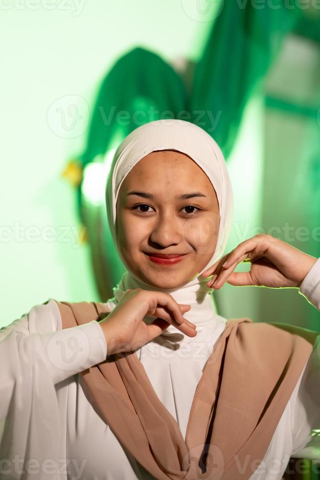 een moslim vrouw in een wit hoofddoek en wit kleren poses met haar handen zonder de minste bedenken Aan haar gezicht en glimlacht gedurende een foto schieten