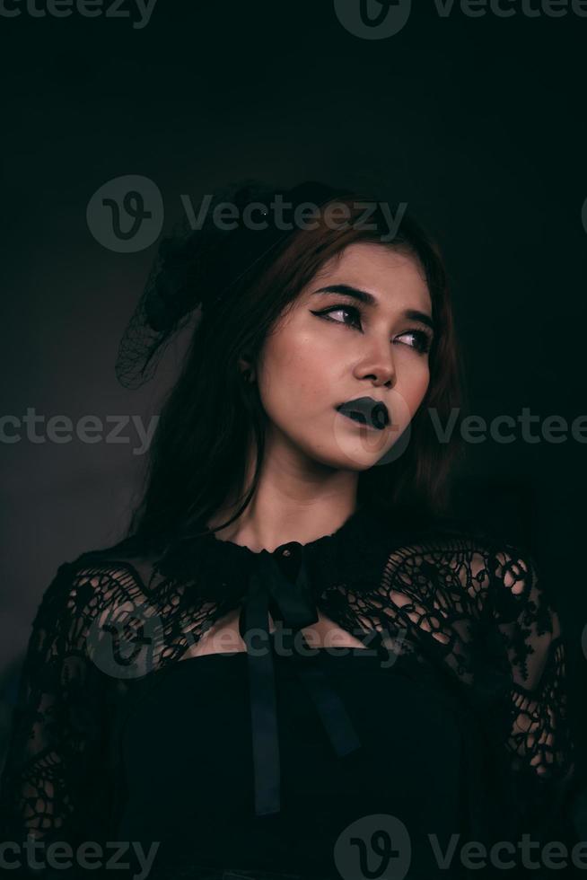 een gotisch Indonesisch vrouw vervelend een mooi zwart hoed terwijl dressing Leuk vinden een heks in zwart foto
