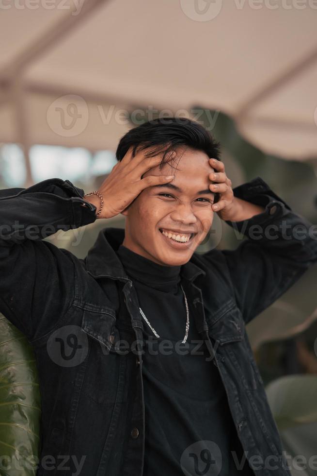 een Aziatisch Mens in een zwart denim jasje poseren met een vrolijk gezicht en heel knap in een cafe foto