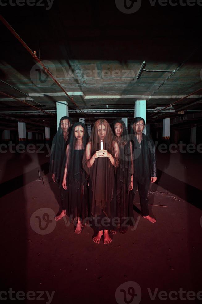 een groep van duivel aanbidders in allemaal zwart kleren en transparant sluiers Holding kaarsen samen gedurende een aanbidden ritueel in een gebouw foto