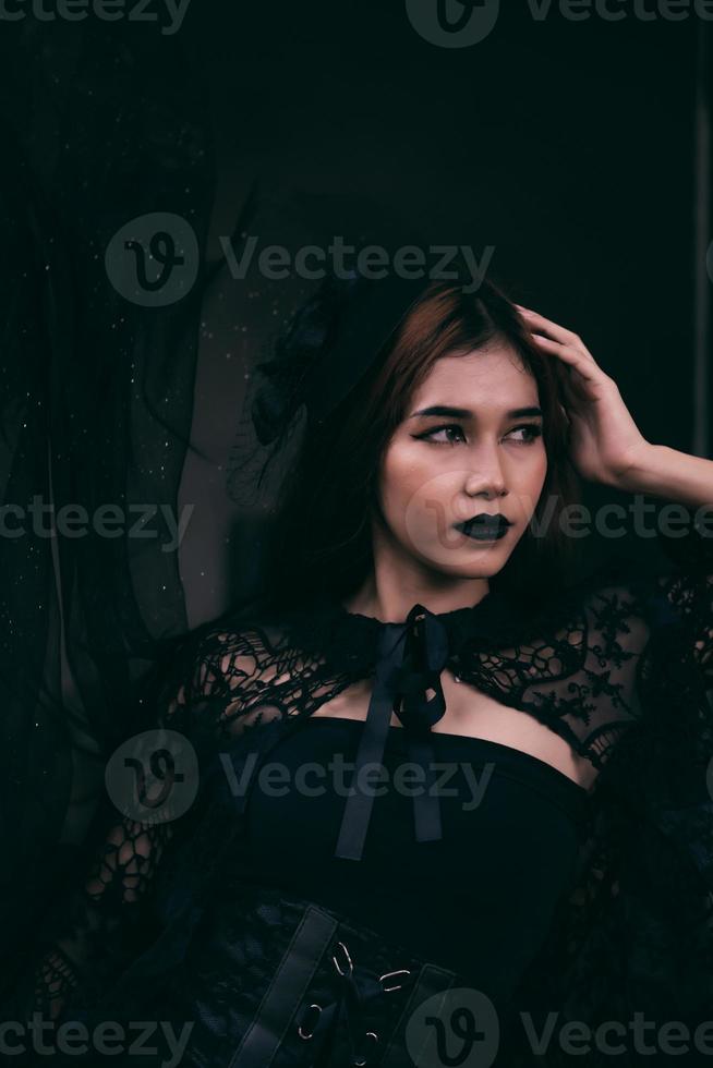 een Aziatisch tiener heeft een eng uiterlijk met helemaal zwart bedenken en een zwart jurk Leuk vinden een heks voordat halloween foto