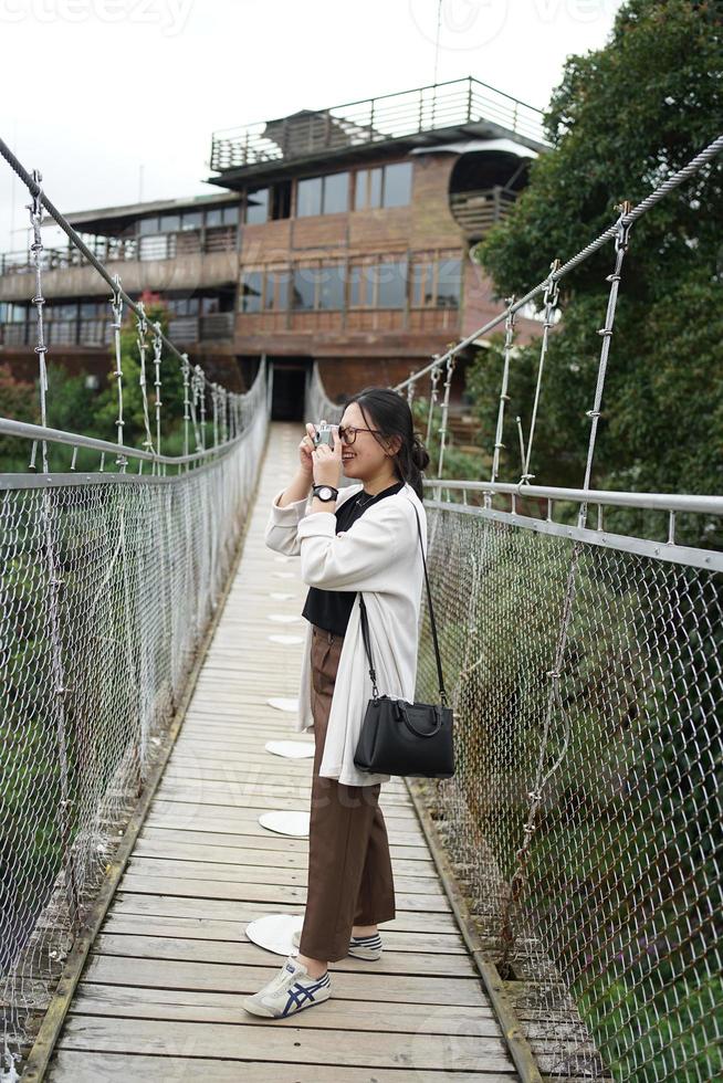 Aziatisch vrouw reiziger staand Aan een geschorst brug foto