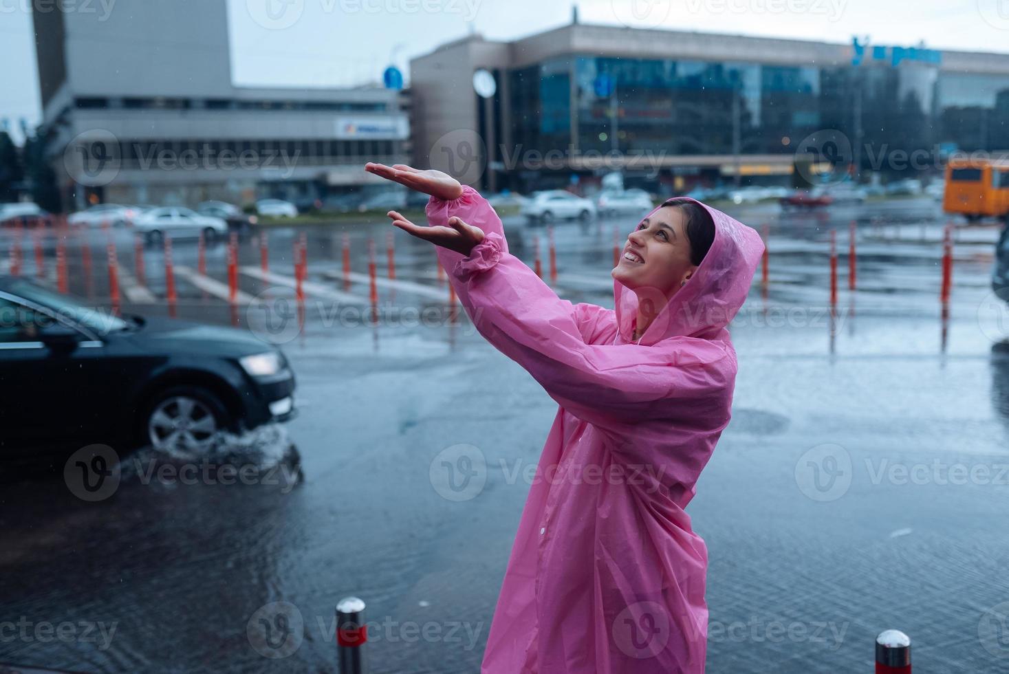 jong glimlachen vrouw in een roze regenjas genieten van een regenachtig dag. foto