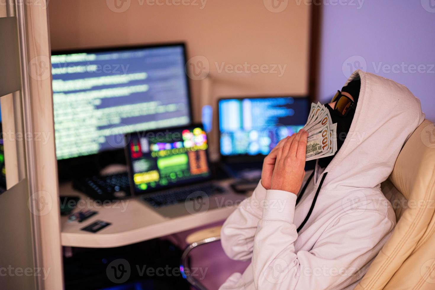 jongen hacker snuift geld dollar. internet diefstal . Mens vervelend een bivakmuts za achter een laptop. foto