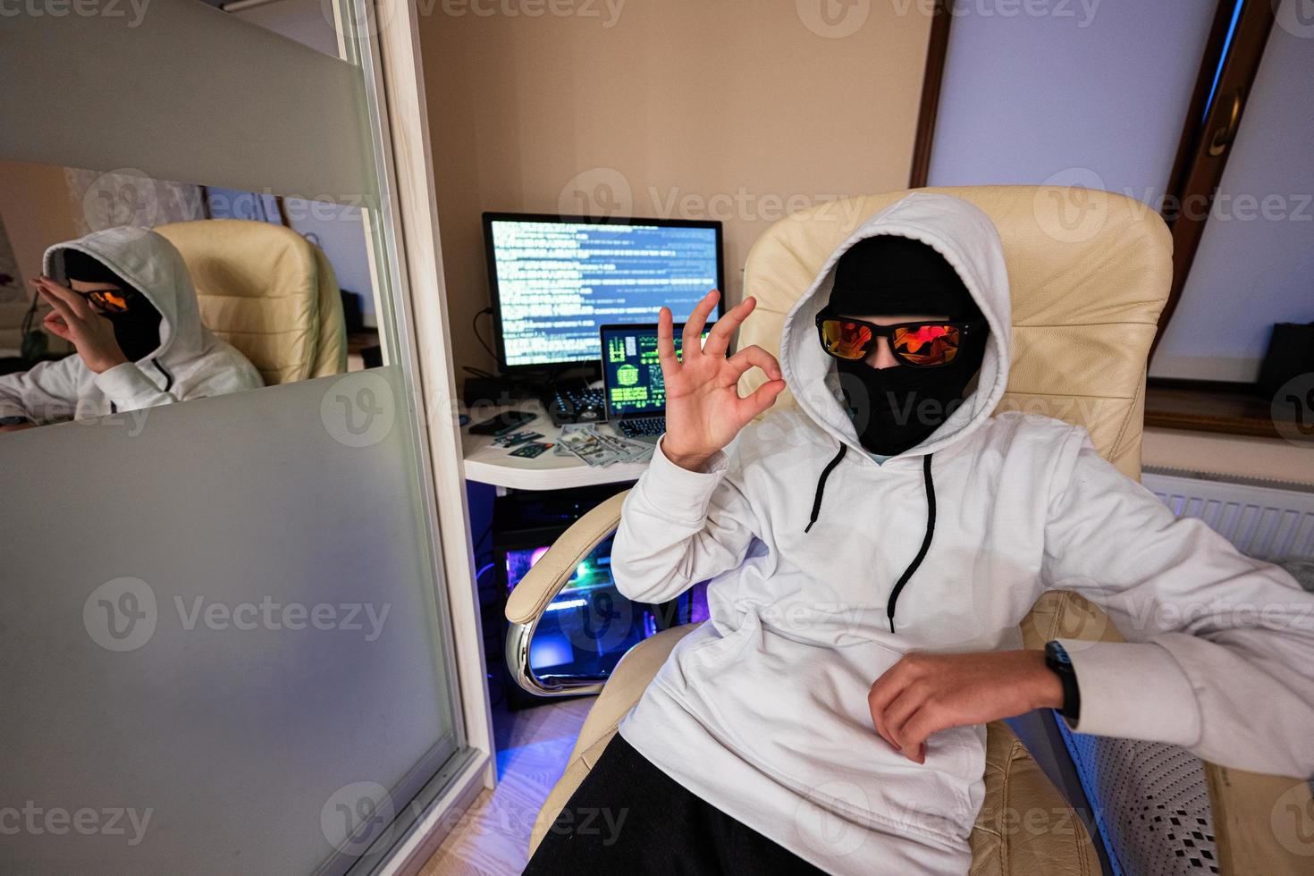 jongen hacker shows OK teken. internet diefstal . Mens vervelend een bivakmuts za achter een laptop. foto