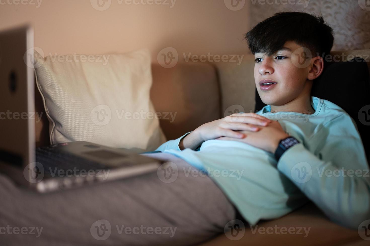 jong tiener jongen in voorkant van een laptop Aan een bed Bij avond. foto