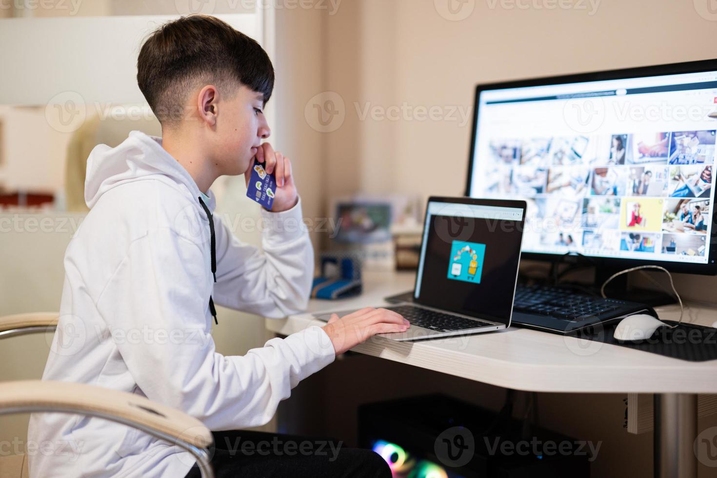 gelukkig tiener- jongen gebruik makend van laptop en credit kaart, zittend Bij bureau en bestellen goederen online van huis. foto