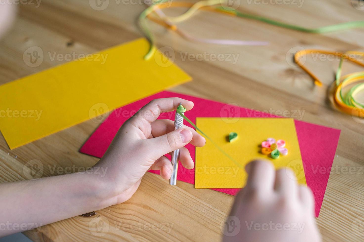 met de handen van een kind, maken een kaart uit van quilling, twist een strip van versmallen papier met een priem foto