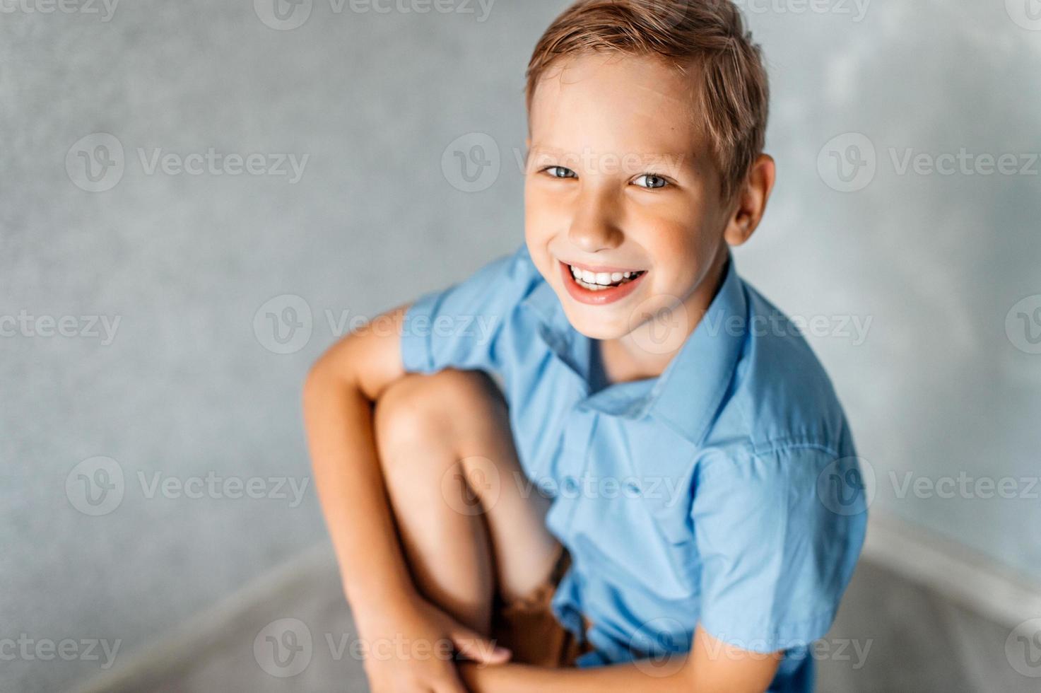 een gelukkig jongen in een blauw overhemd is zittend Aan een stoel foto