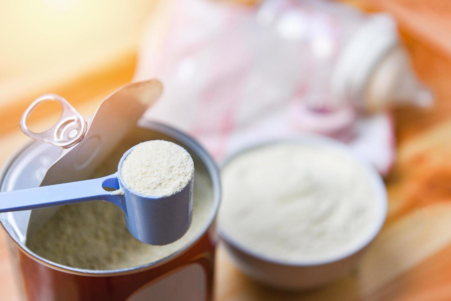 melk poeder in lepel met kan en baby fles melk in kom Aan houten tafel foto