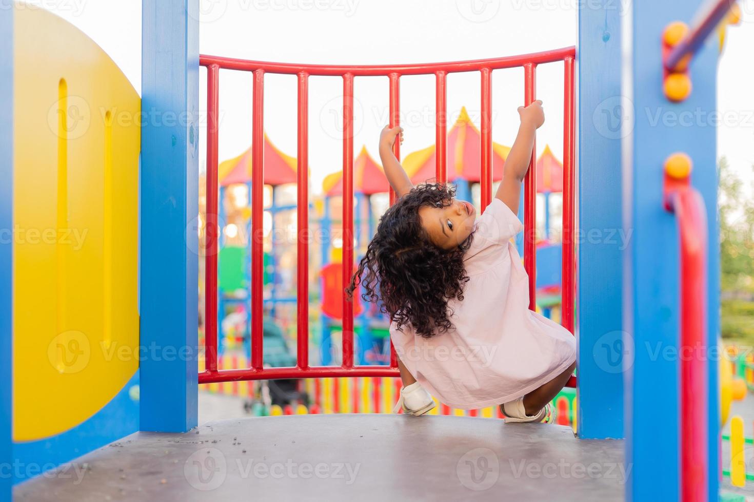 donker baby met gekruld haar- in een pale roze jurk Toneelstukken Aan een straat speelplaats en ritten naar beneden de heuvel. de concept van een gezond levensstijl. gelukkig jeugd. hoog kwaliteit foto