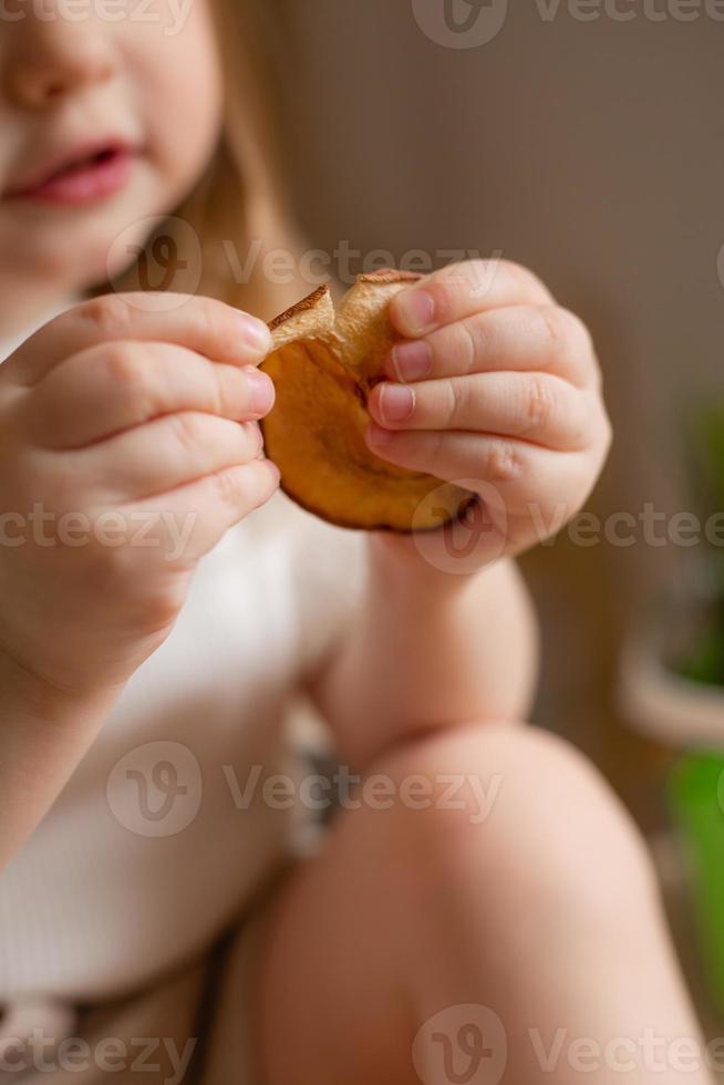 schattig weinig meisje eet natuurlijk pastille Bij huis in een houten keuken. voedsel voor kinderen van natuurlijk producten foto