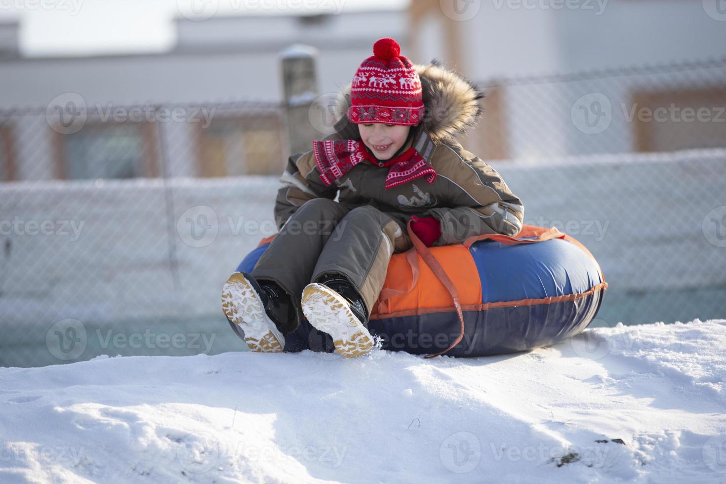 een gelukkig jongen omhoog in de lucht Aan een buis rodelen in de sneeuw.. een jongen dia's naar beneden een heuvel in winter. foto