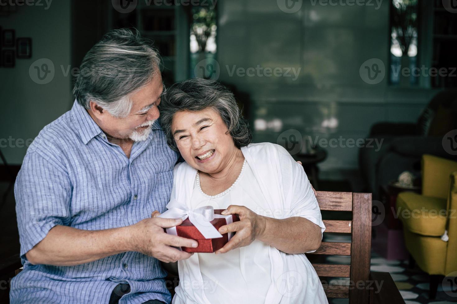 lachende senior man verrassing geven geschenkdoos aan zijn vrouw foto