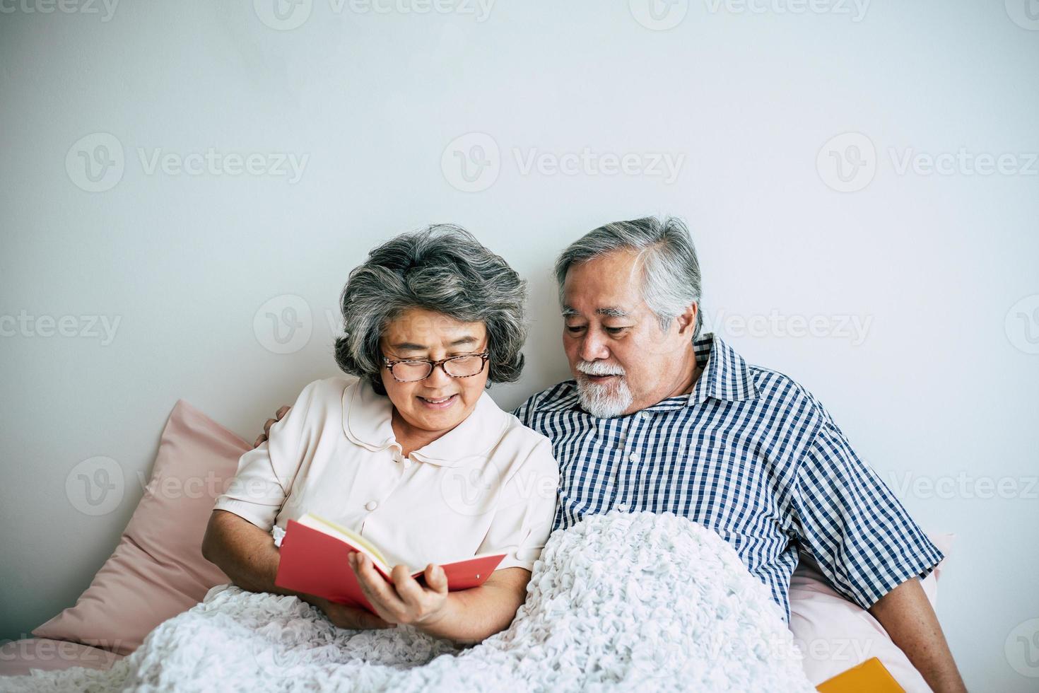 bejaarde echtpaar liggend op het bed en lezen van een boek foto