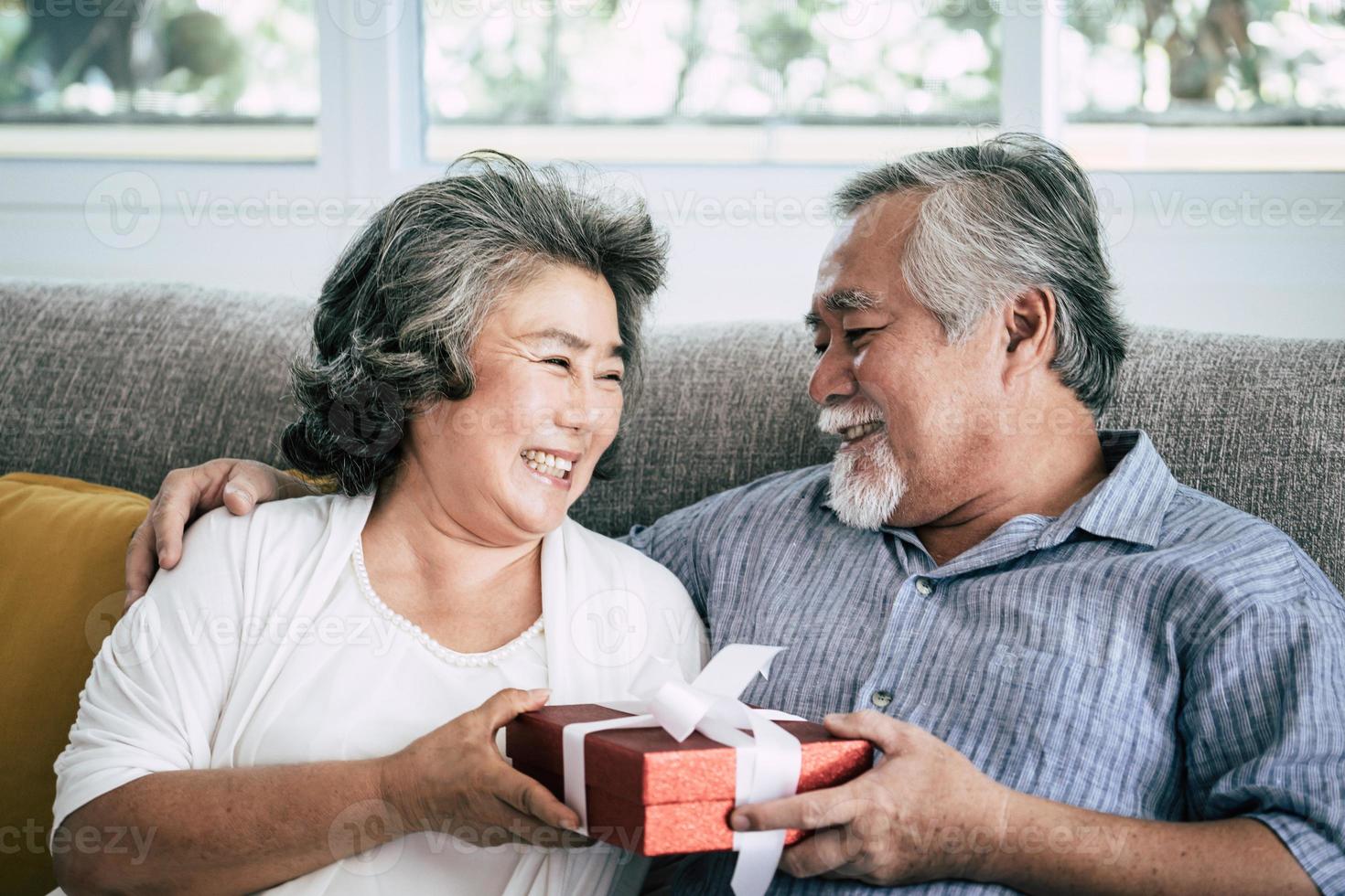 bejaarde echtpaar met verrassing geschenkdoos in de woonkamer foto