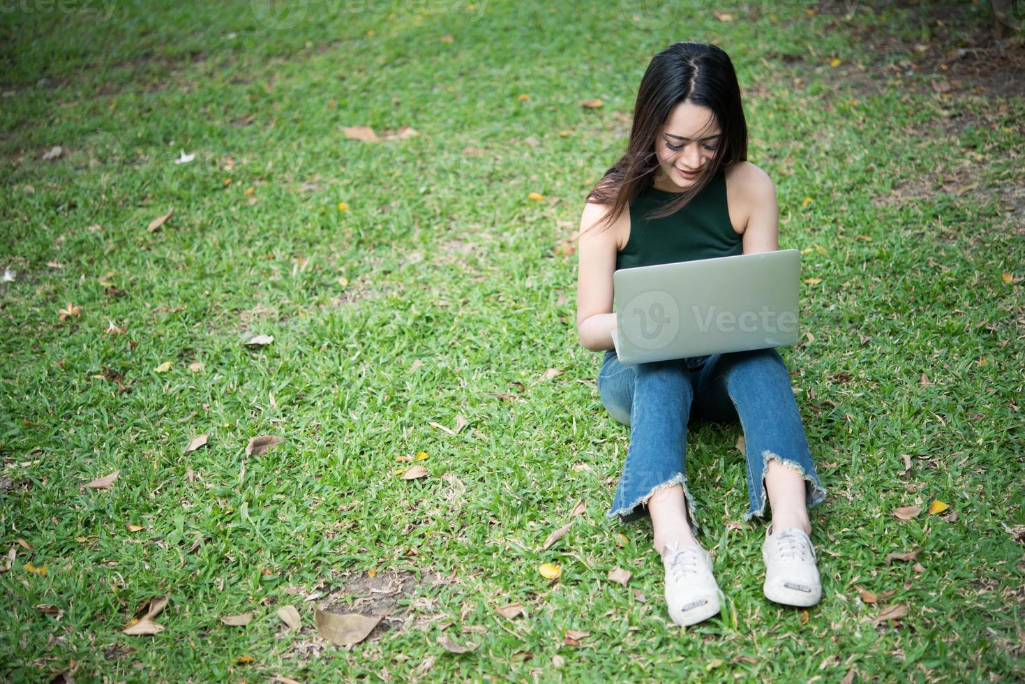 jonge mooie vrouw zittend op het groene gras en met behulp van laptop in het park foto