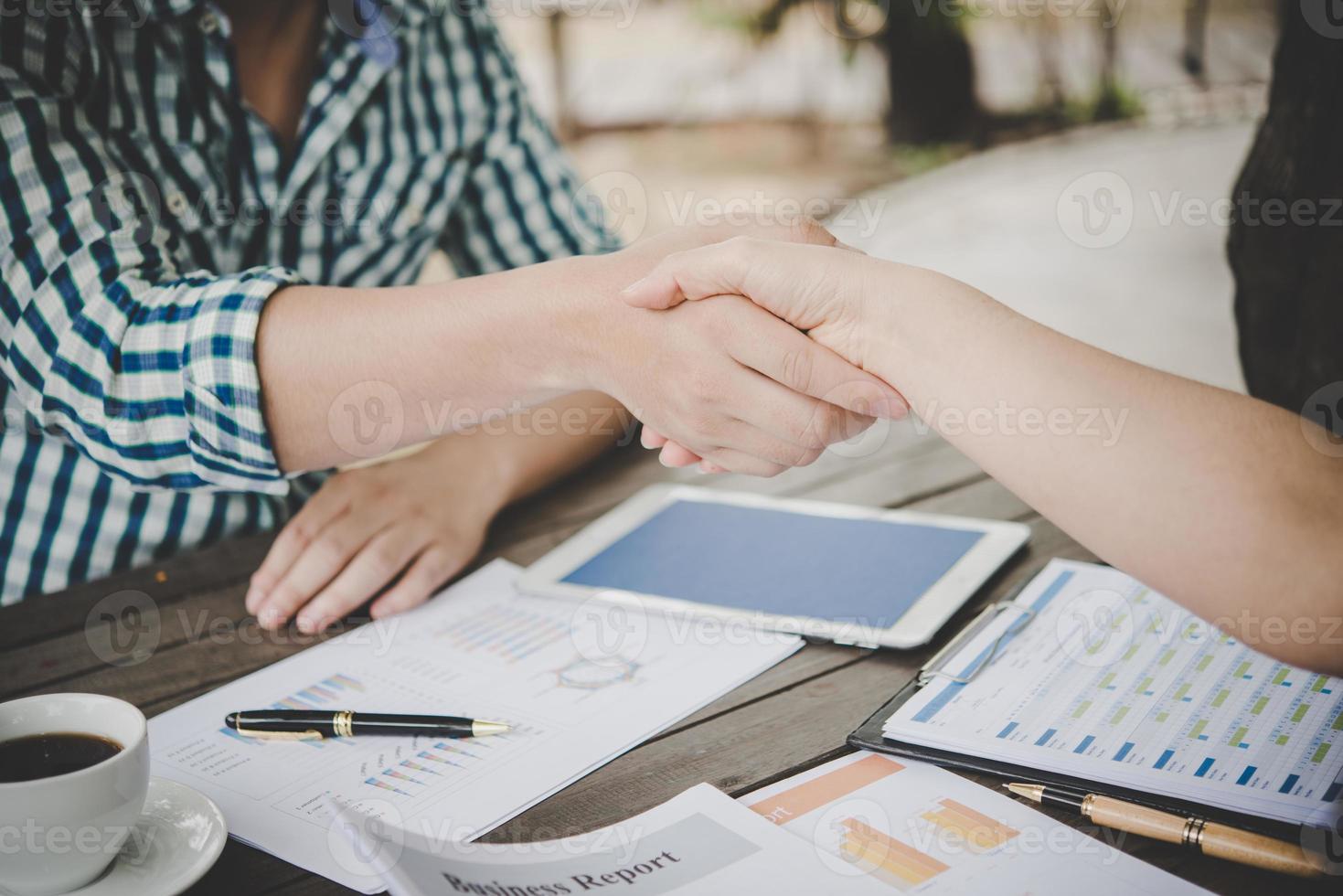 close-up van twee zakenmensen handen schudden zittend op de werkplek foto