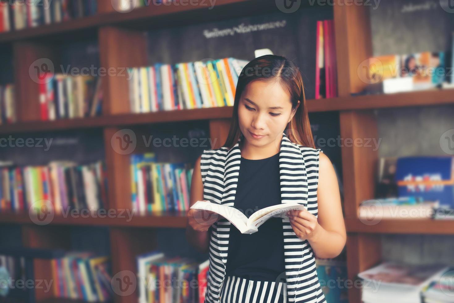 Aziatische vrouw die een boek in bibliotheek leest foto