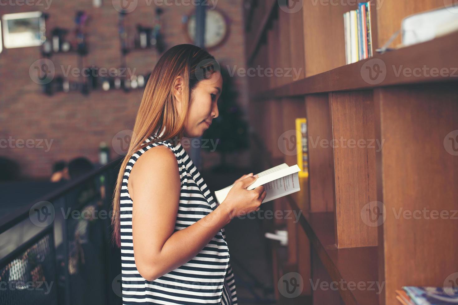 Aziatische vrouw die een boek in bibliotheek leest foto