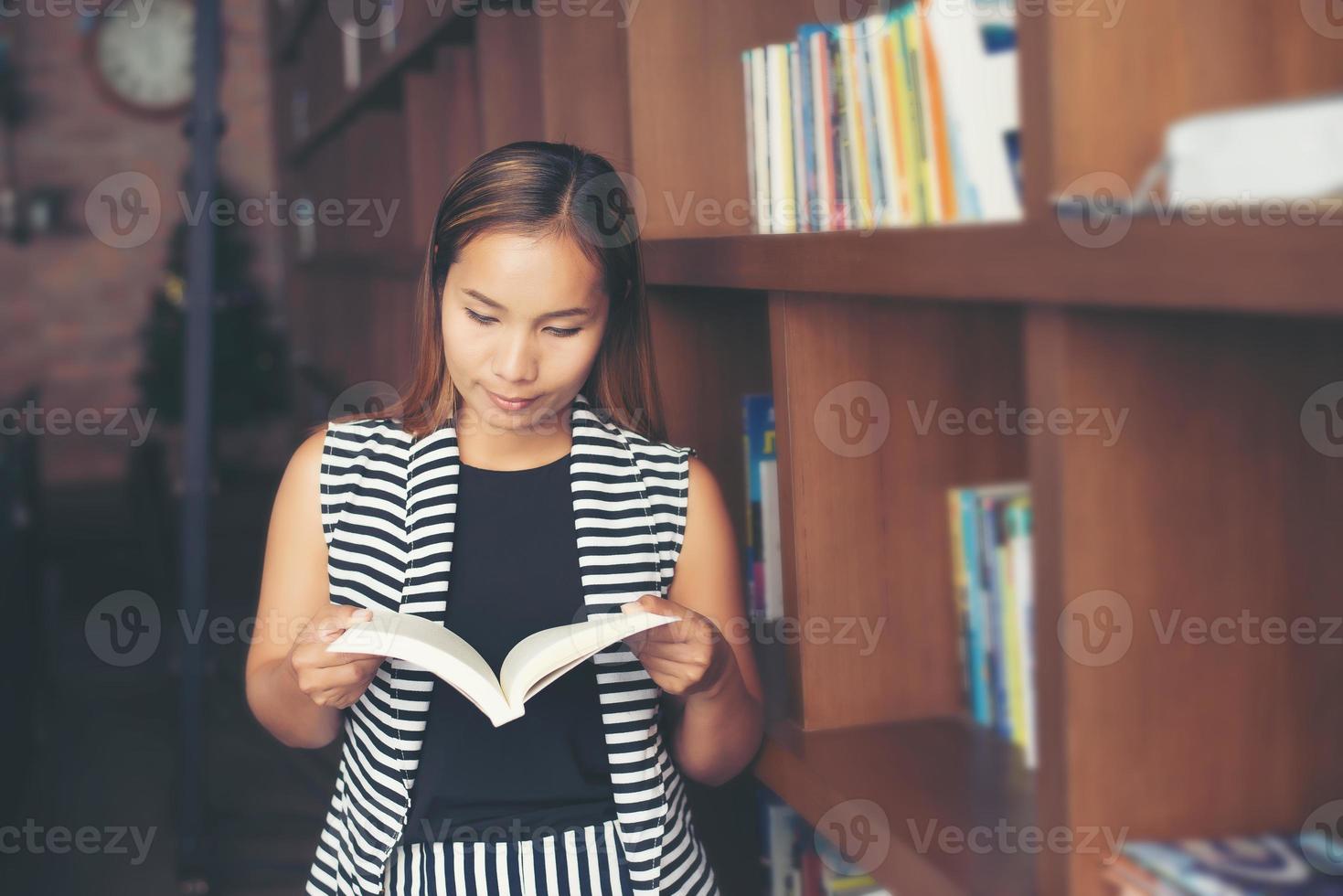 Aziatische vrouw die een boek in bibliotheek leest foto