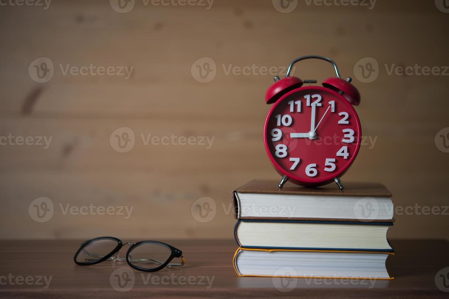 wekker om 9 uur op stapel boeken met bril op houten tafel foto