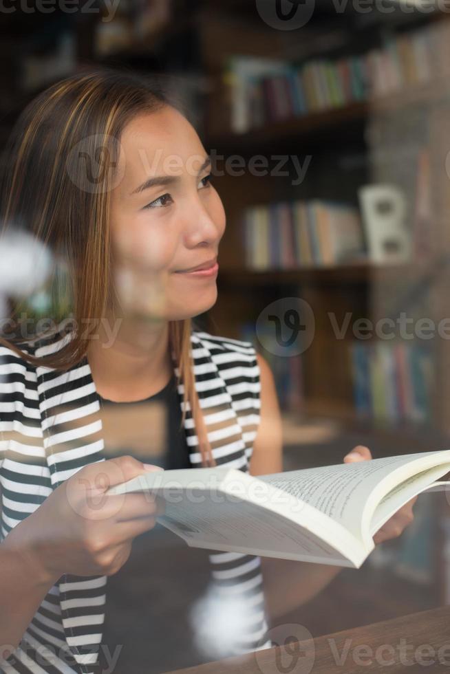 Aziatische vrouw die een boek in bibliotheek leest foto