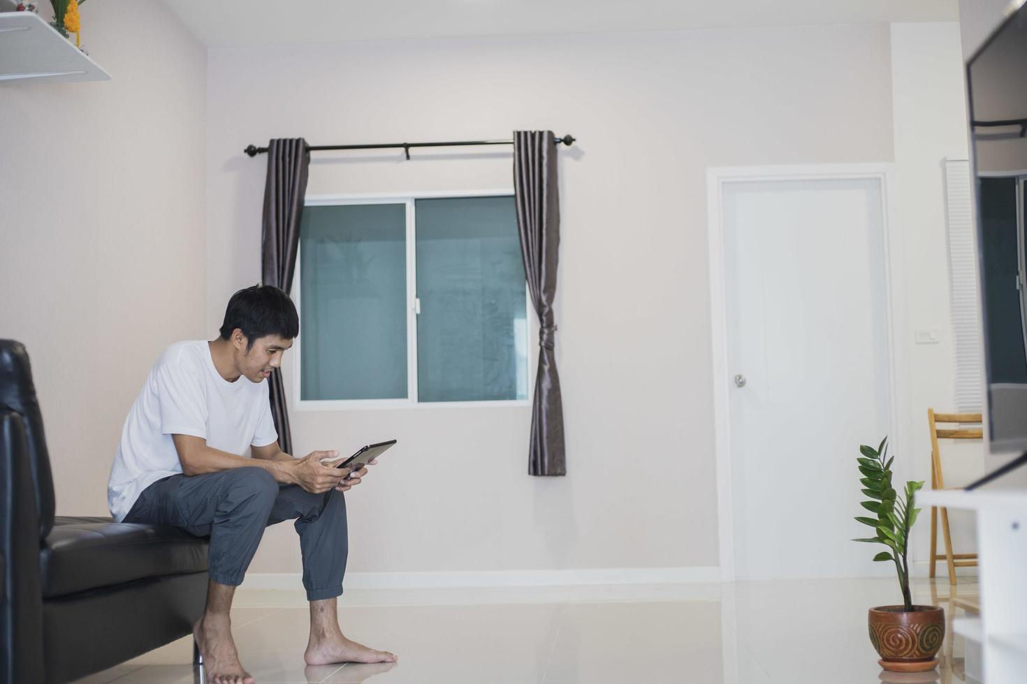 Aziatische man met tablet thuis op de bank foto