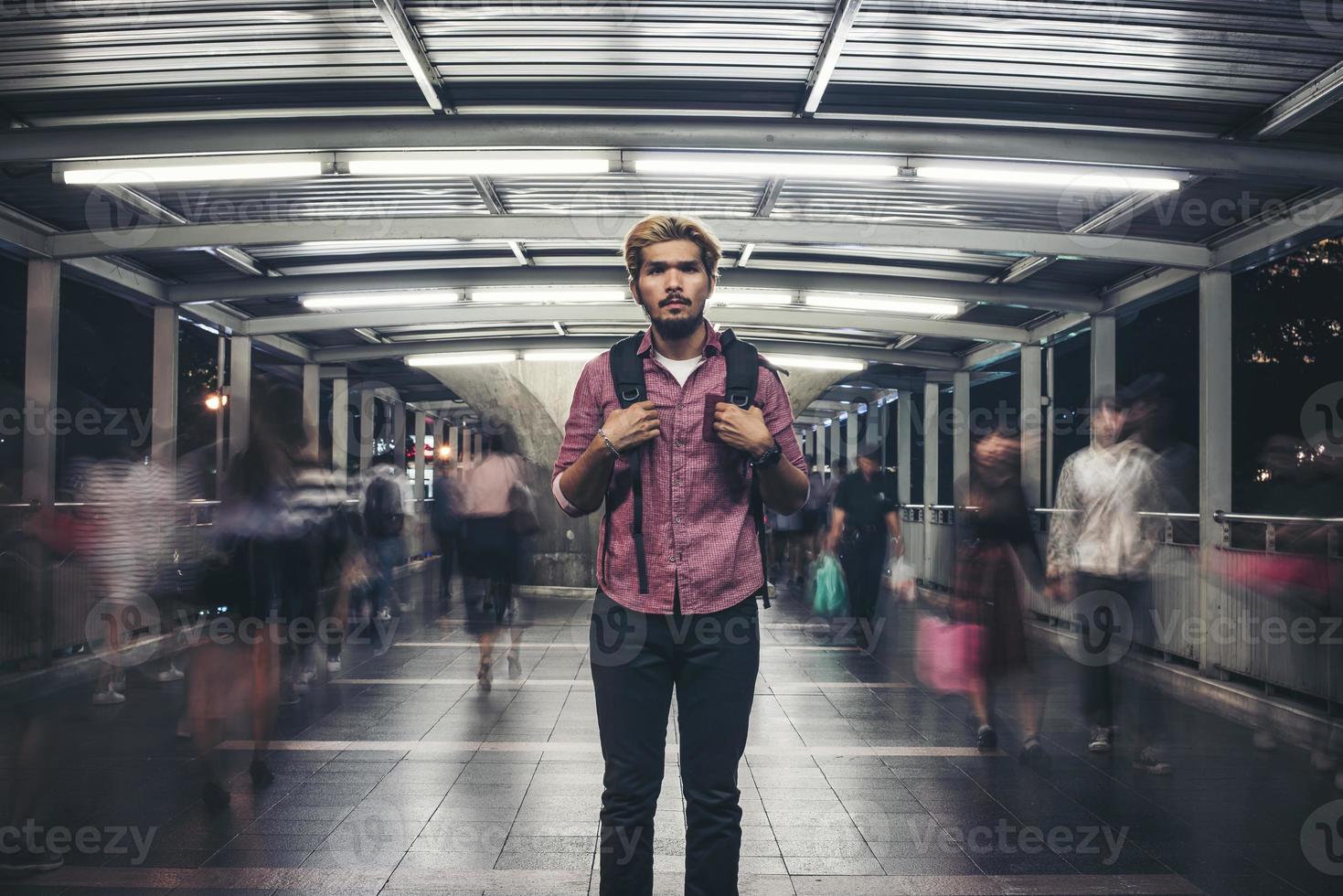 knappe bebaarde man met rugzak staande op straat tijdens het reizen 's nachts foto
