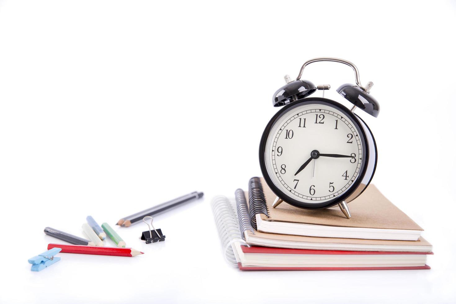 een stapel boeken met gekleurde pen en wekker op witte achtergrond foto