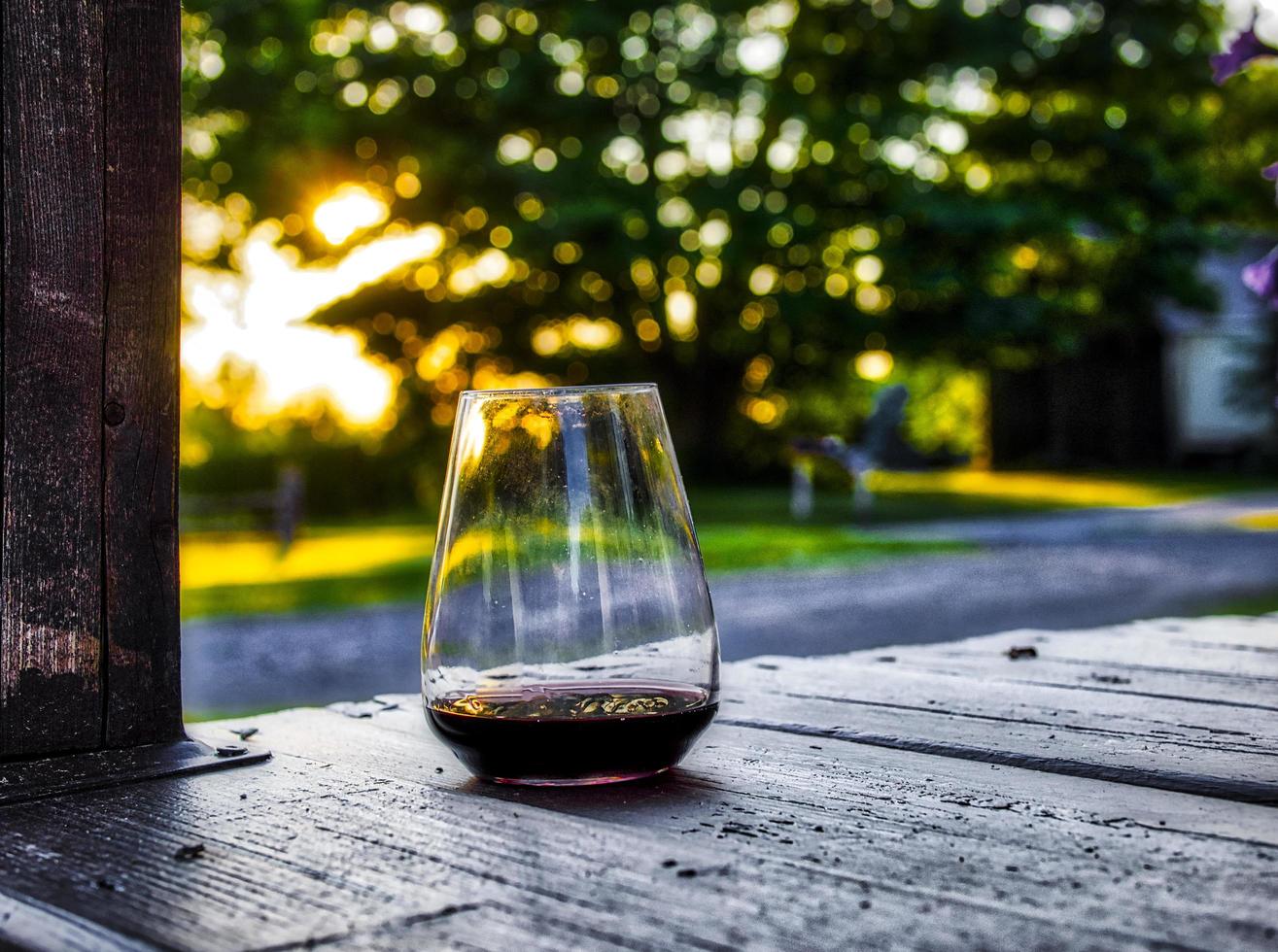 glas wijn verlicht op een veranda met bomen en tuin op de achtergrond bij zonsondergang foto