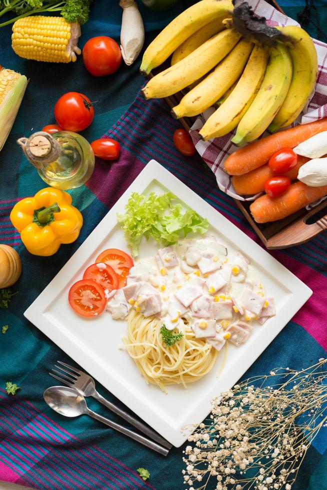 pasta carbonara met spek en Parmezaanse kaas op een witte plaat met groenten op kleurrijk tafelkleed foto