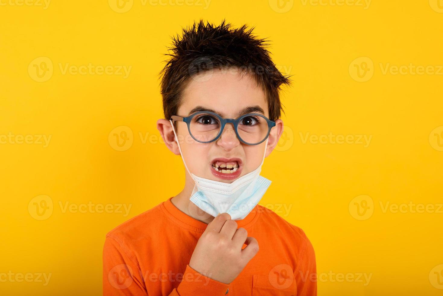 portret van een boos kind dat willen verwijderen gezicht masker voor covid-19 coronavirus. geel achtergrond foto