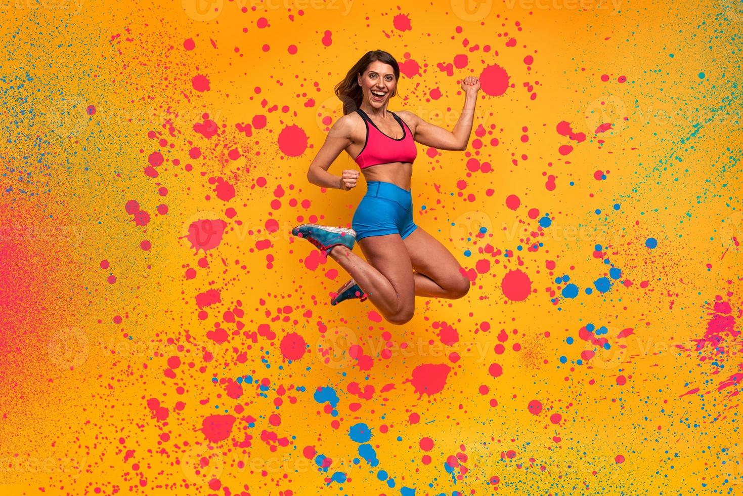 sport vrouw springt Aan een geel achtergrond. gelukkig en blij uitdrukking. verstuiven effect foto