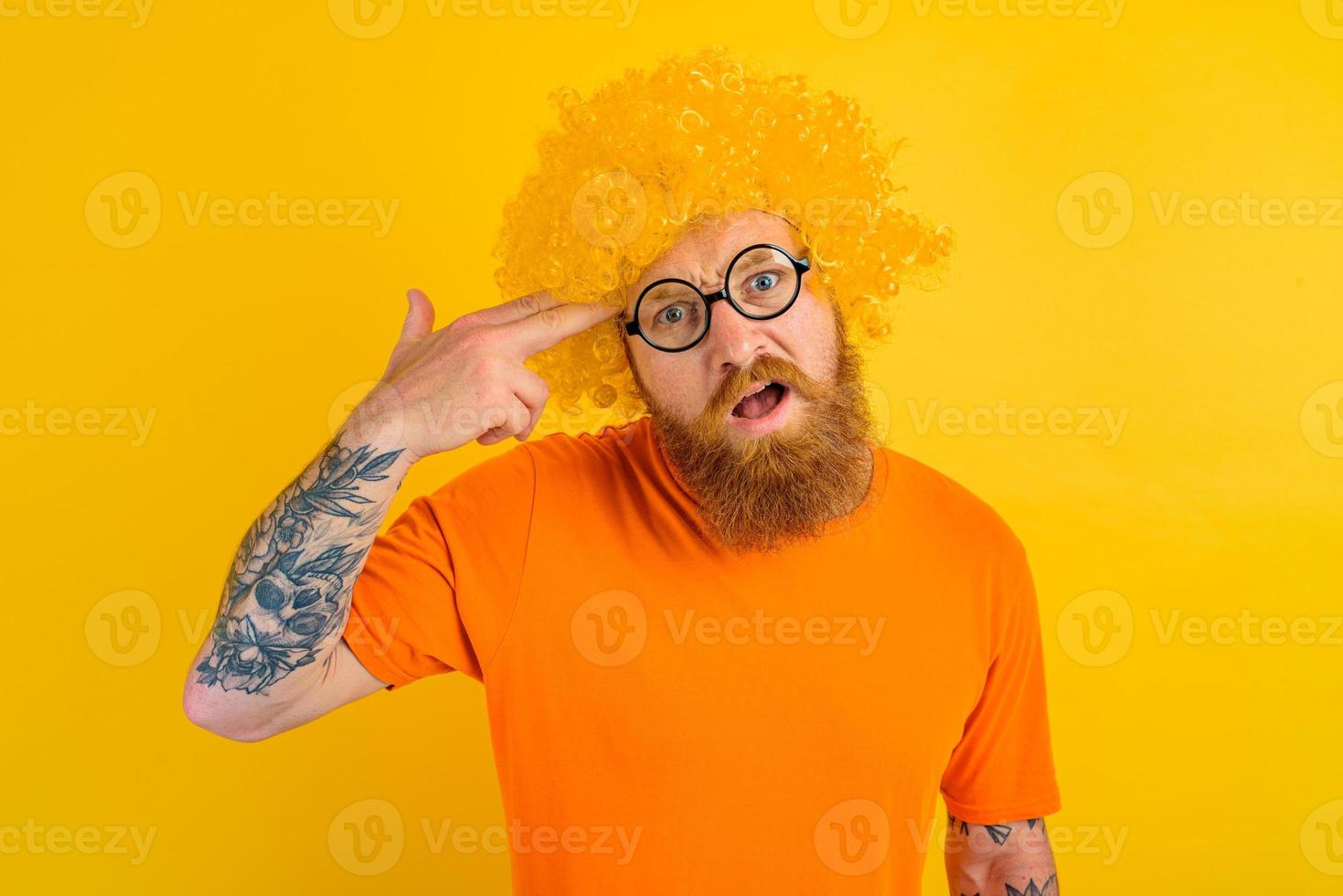 Mens met baard, geel pruik en bril doet een geweer gebaar met de hand- foto