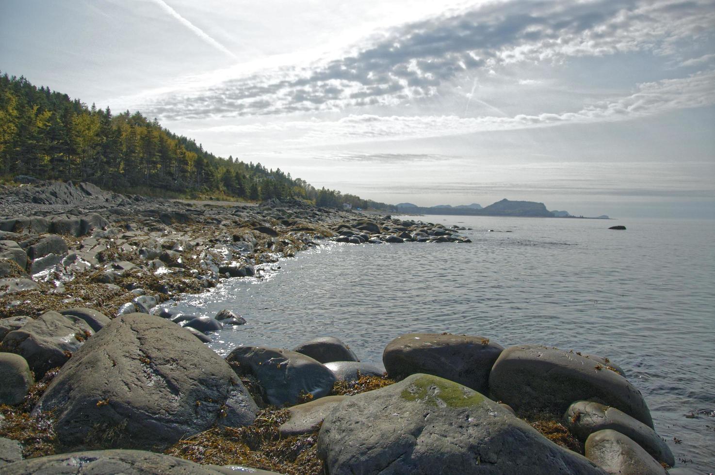 rotsen en kustlijn naast waterlichaam met bewolkte blauwe hemel in Quebec, Canada foto