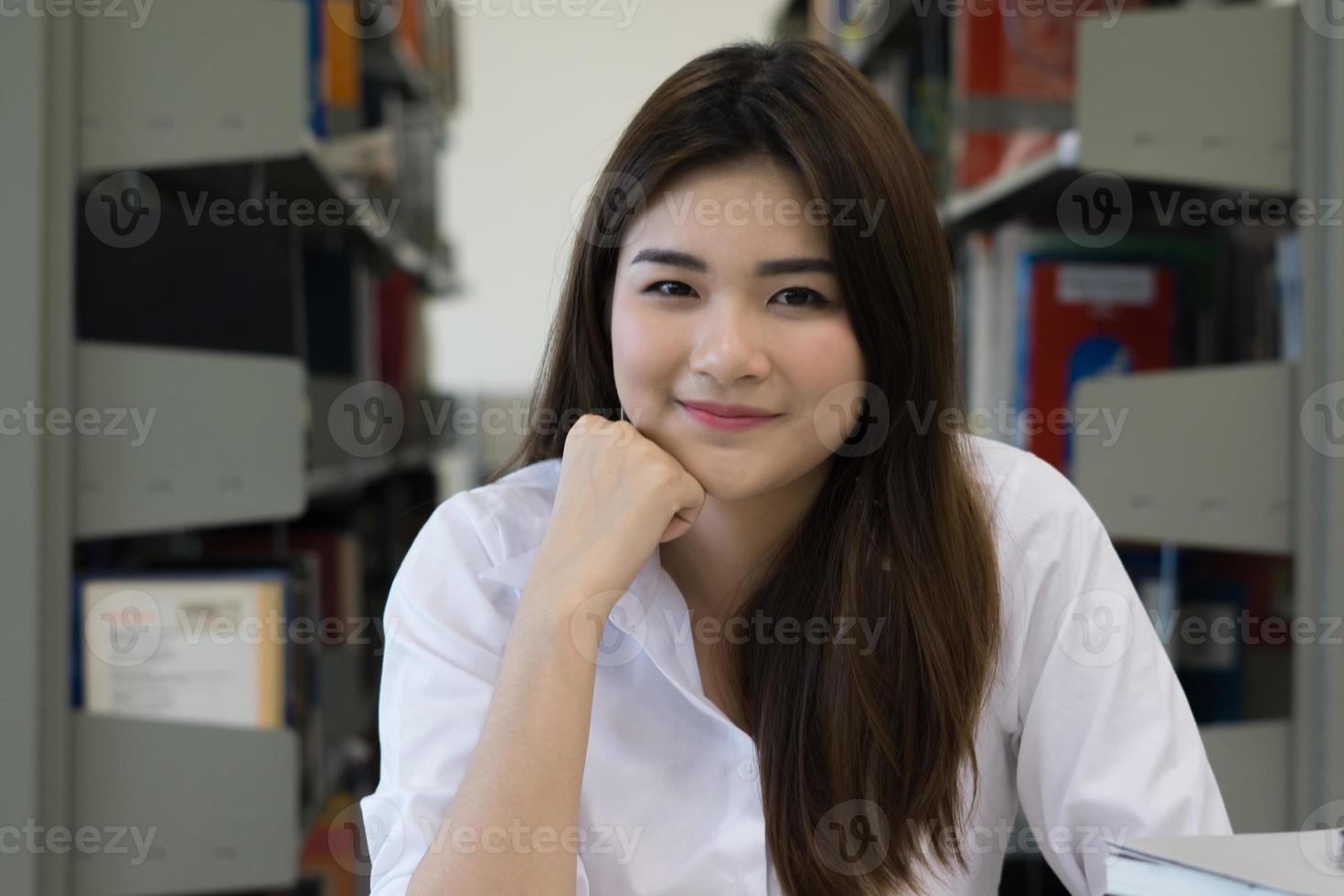 jonge mooie Aziatische student lachend tijdens het lezen in de bibliotheek foto