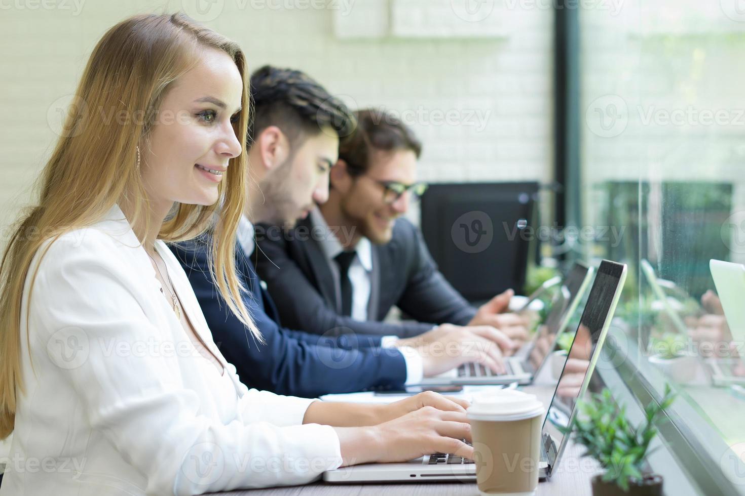 zakenvrouw met behulp van laptop om te werken, terwijl collega's op de achtergrond communiceren foto