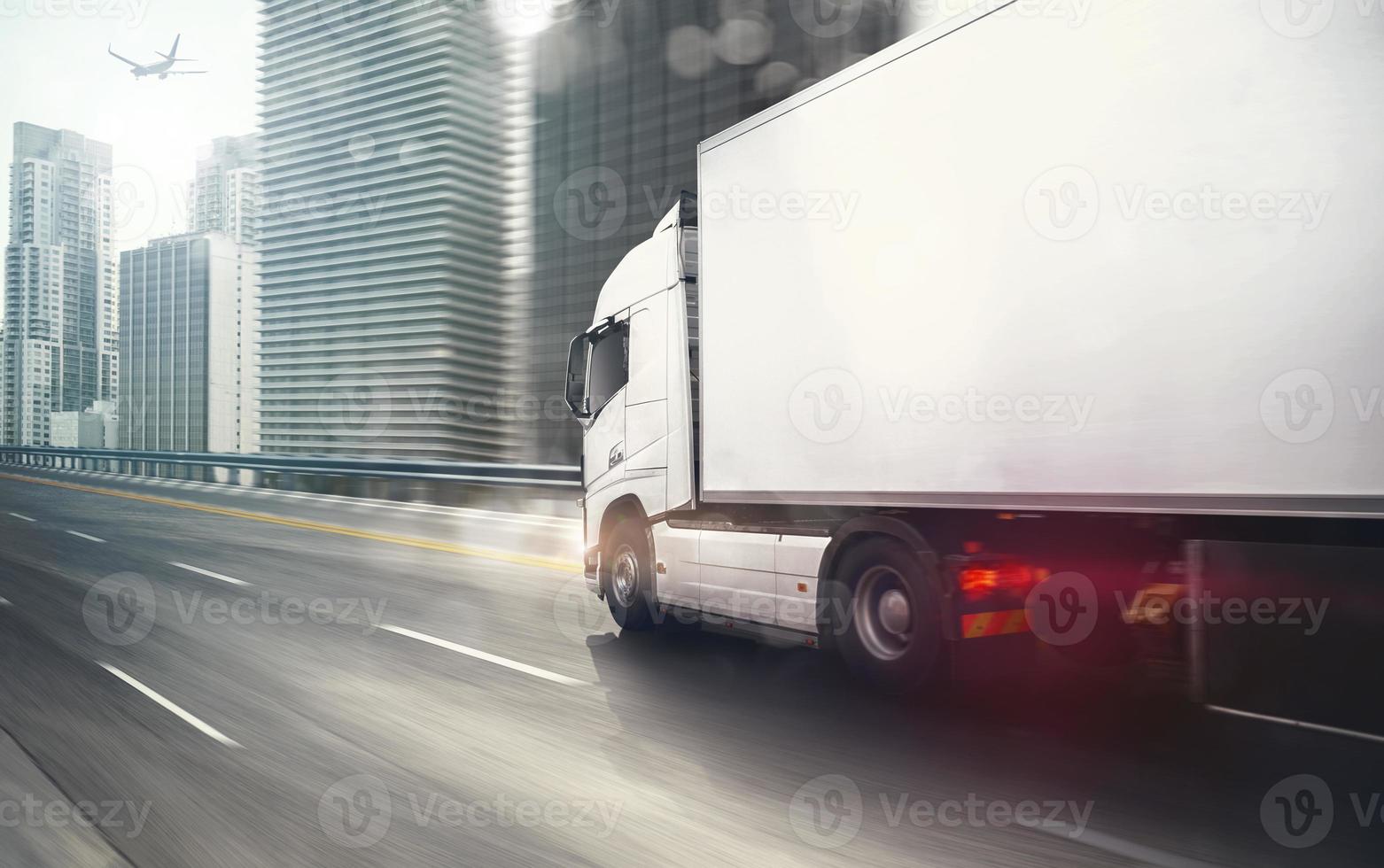 wit vrachtauto in beweging snel Aan de snelweg met een modern stad in de achtergrond foto