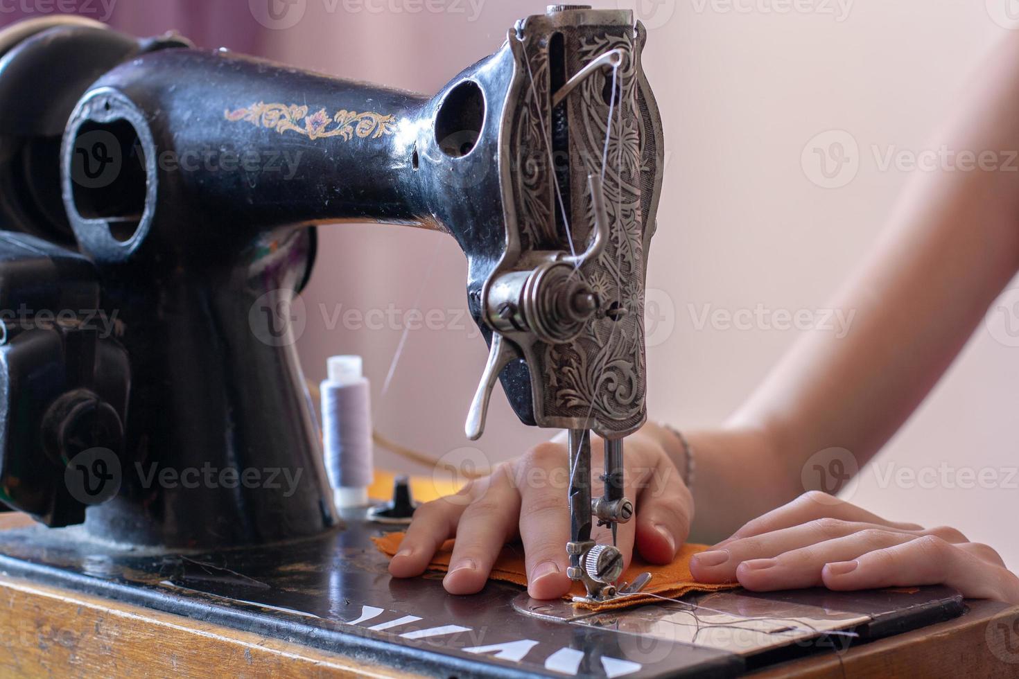 naaister naait Aan een oud retro naaien machine. handen zijn Aan de kleding stof. dichtbij omhoog naaien werkwijze. Ondiep diepte van veld. focus Aan de handen. horizontaal. foto