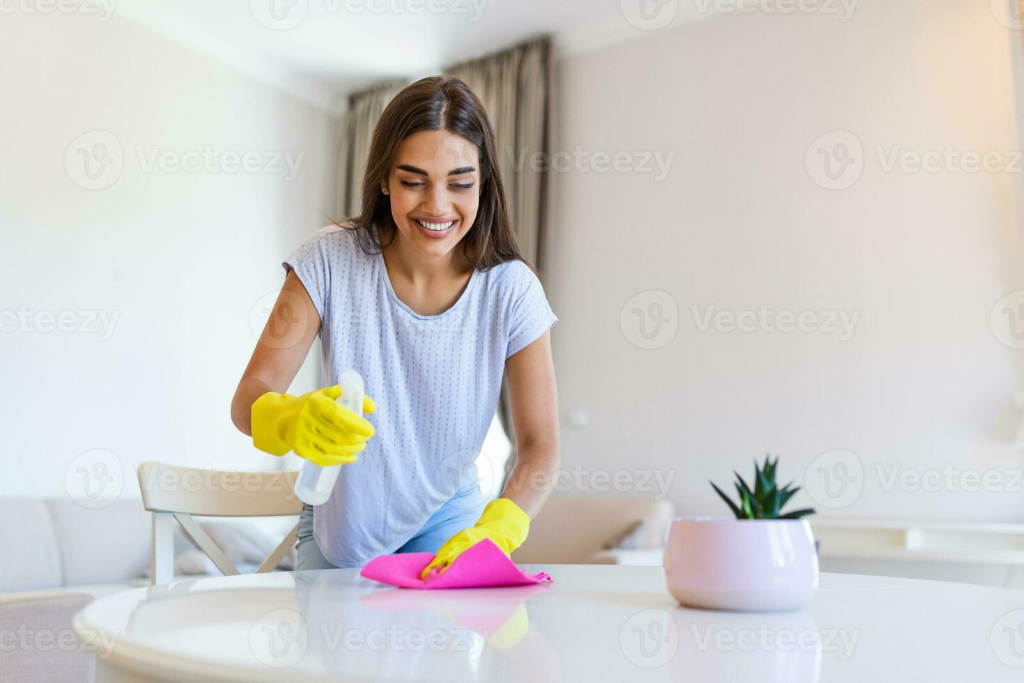 vrouw vervelend geel rubber beschermend handschoenen en schoonmaak wit tafel. gelukkig vrouw huishoudster schoonmaak de huis foto
