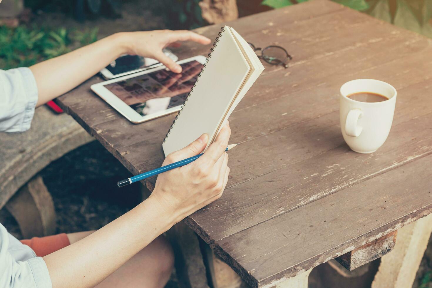 hand- vrouw gebruik makend van tablet en Holding notitieboekje Aan tafel hout Bij koffie winkel. foto