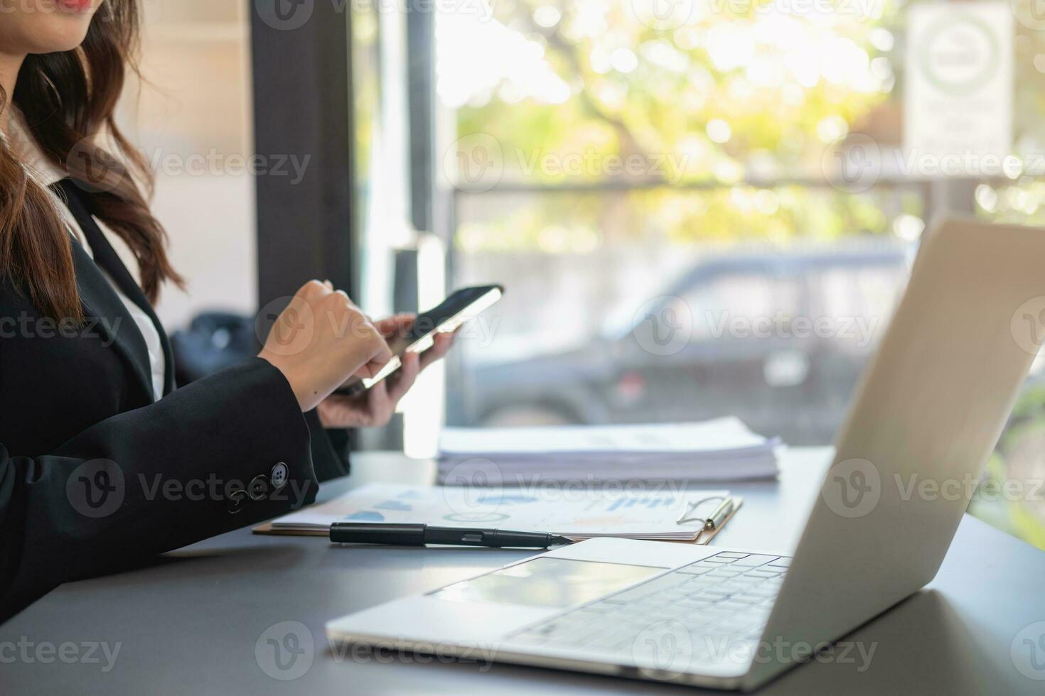 Aziatisch zakenvrouw in zwart pak gebruik makend van een mobiel telefoon naar communiceren met klanten naar verslag doen van leven verzekering onkosten en opname van oom laptop binnen kantoor Gezondheid verzekering concept foto